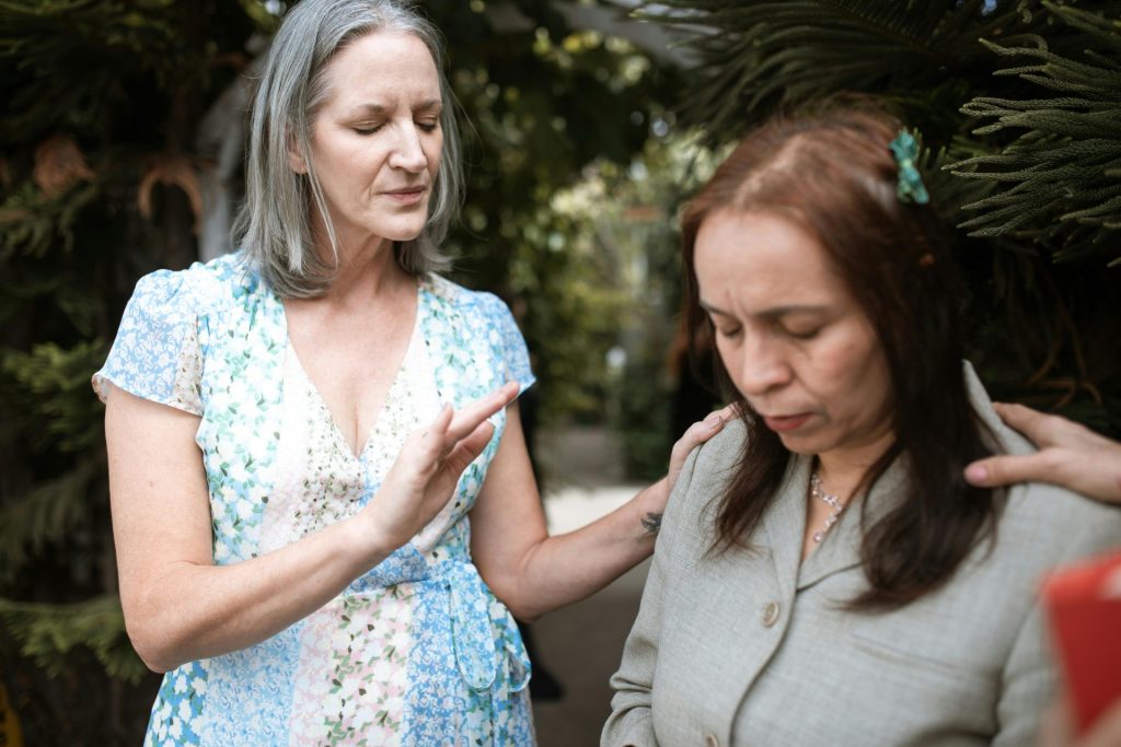 Two women in a peaceful prayer moment, sharing spiritual connection outdoors.